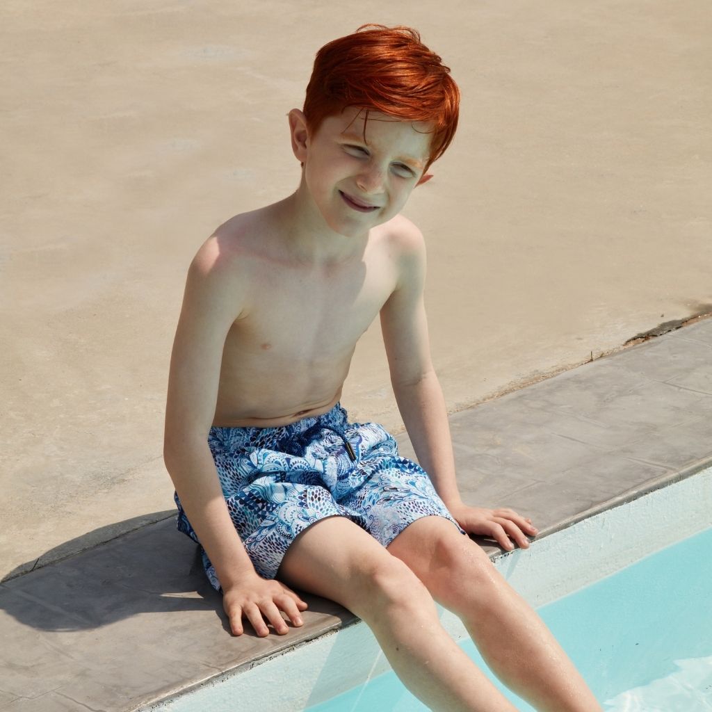 Little boy by the pool wearing the Marie Raxevsky boys swim shorts in Wave print