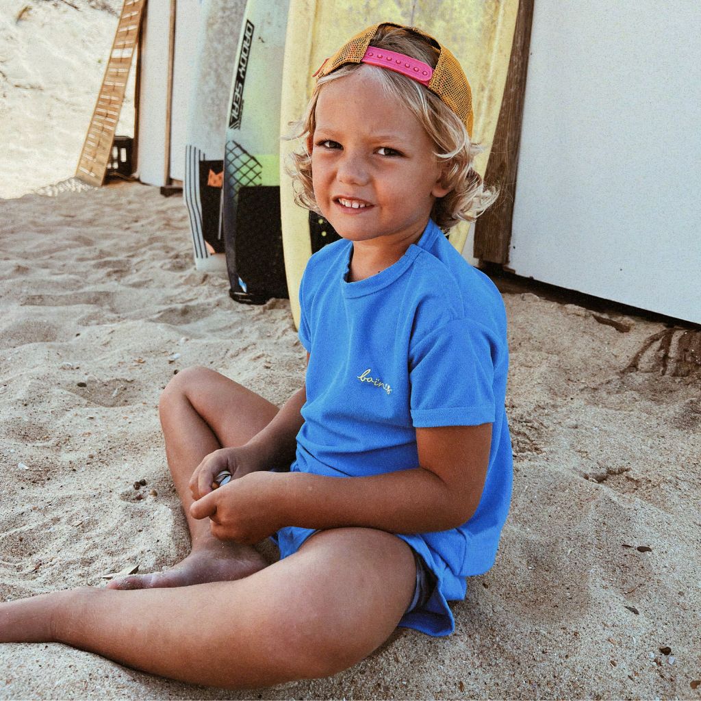 Little boy sitting in the sand wearing the Mike beach wear set in blue from Baines Collection