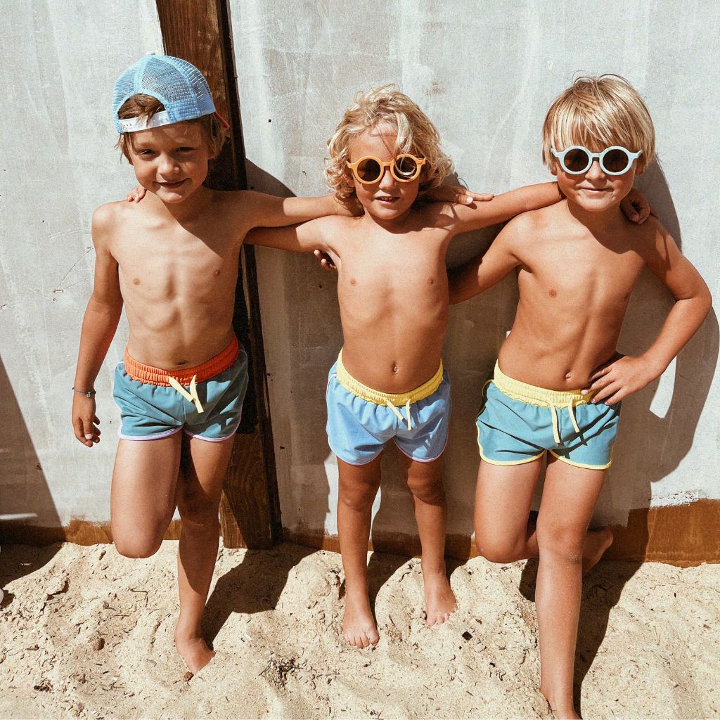 Little boys on the beach wearing the Kiwi Unisex Swim Shorts in Blue Java from Baines Collection
