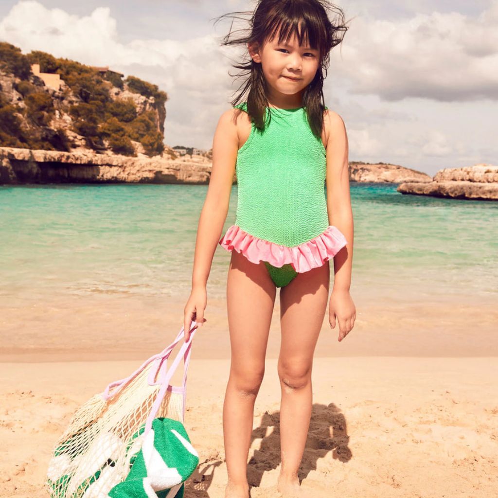 Little girl on the beach wearing the Hunza G Baby Duo Denise swimsuit in lime and bubblegum featuring the original crinkle