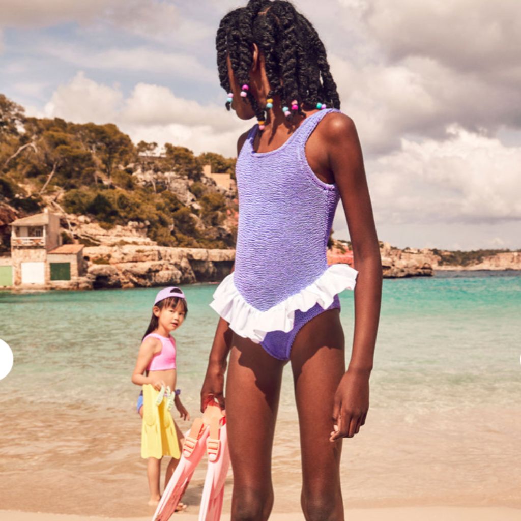 Little girl on the beach wearing the Hunza G Kids Denise Swimsuit in Lilac