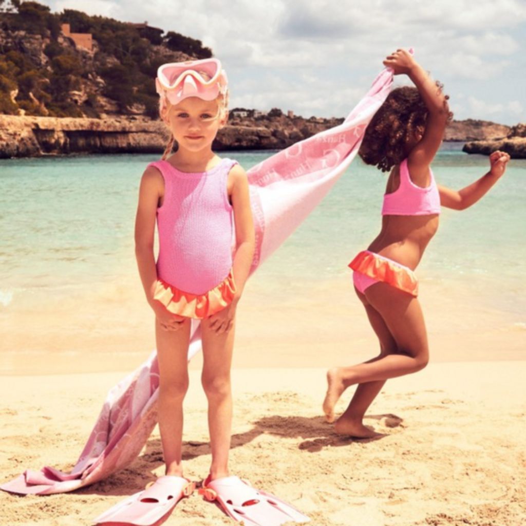 Little girls on the beach wearing the Hunza G Baby Duo Olive Bikini in Bubblegum and Orange