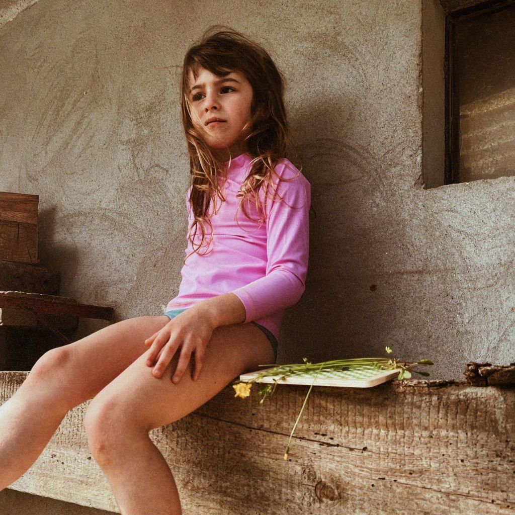 Little girl wearing the Papaya rash vest in Marshmallow Pink from Baines Collection