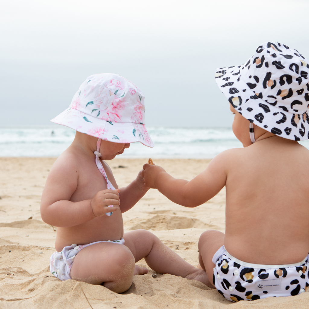 Children on the beach wearing Anchor & Arrow Leopard print and Pretty Peony unisex reusable swim hats and swim nappy