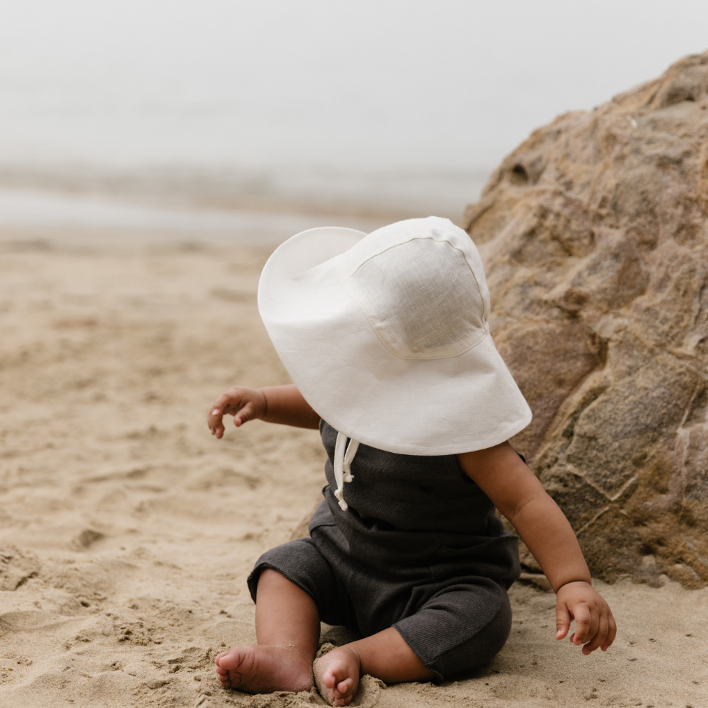 Baby boy on the sand wearing Briar Baby sun hat in oyster white 