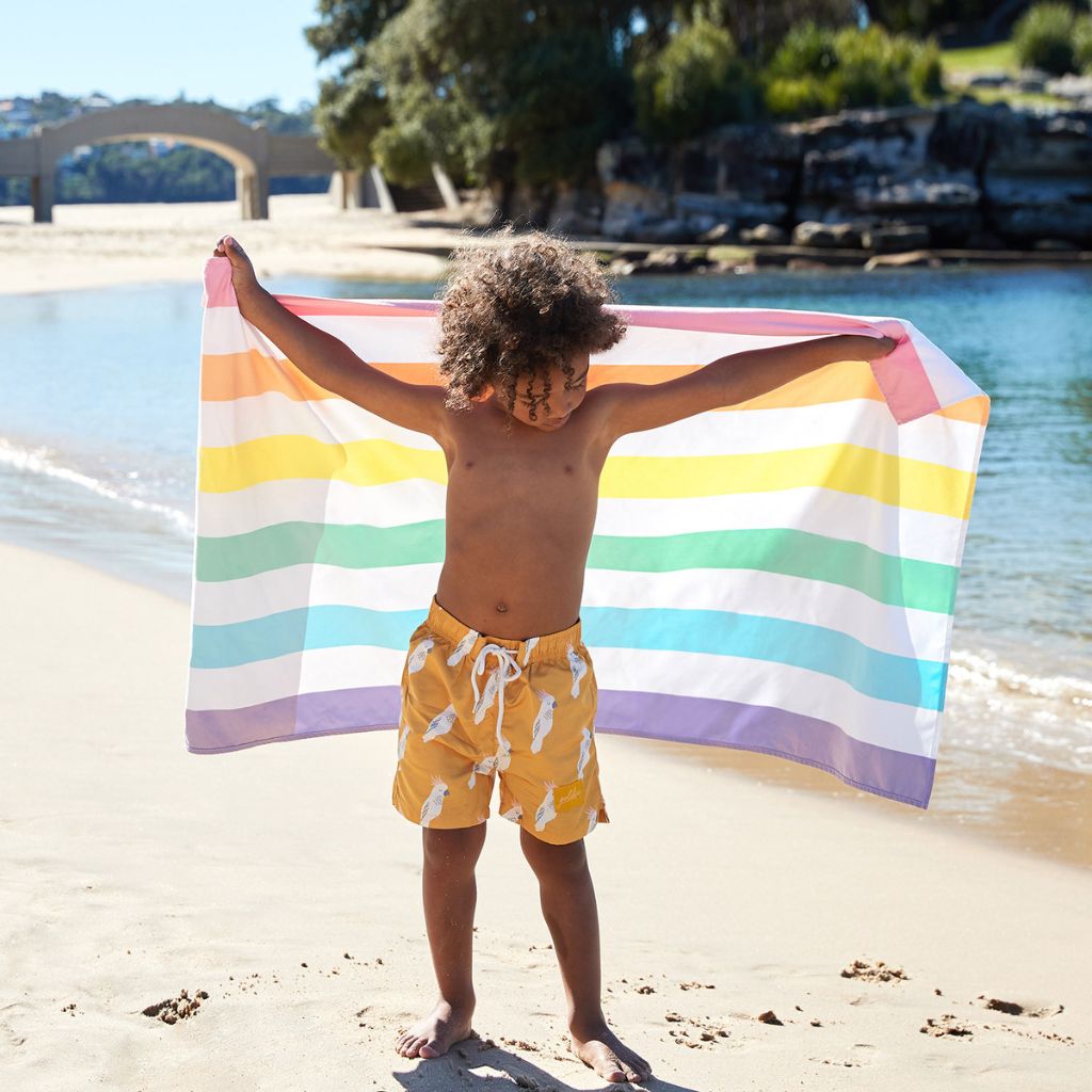 Little boy holding Dock and Bay Striped Summer Beach towel in Unicorn Waves print
