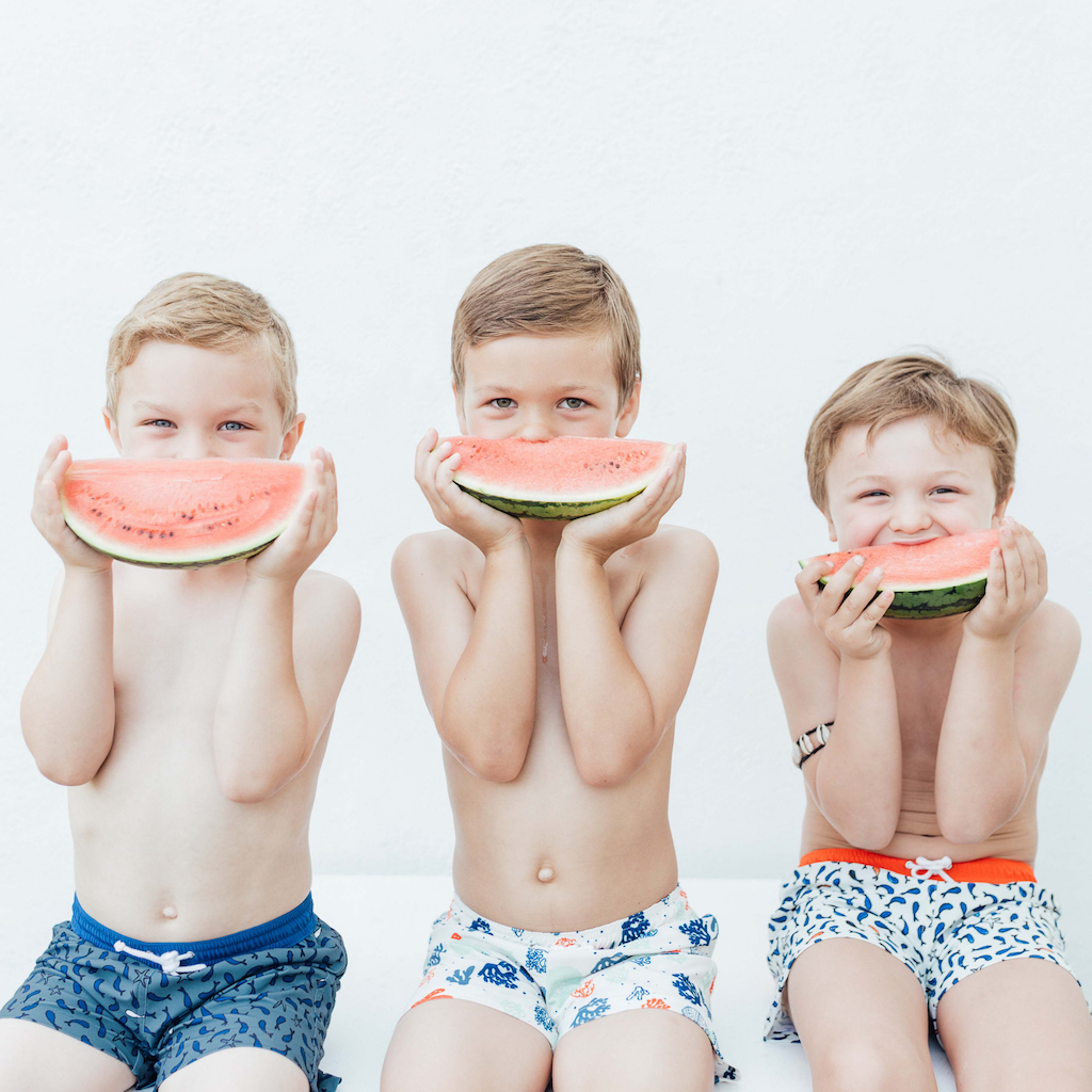 Boys wearing Folpetto Tommaso swim shorts for boys in orange, blue and green coral print