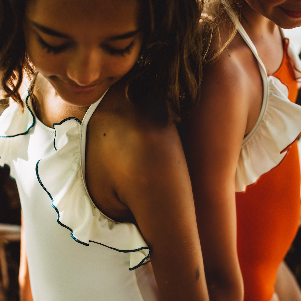 Friends in matching Folpetto linda halterneck girls swimsuit with ruffles in cinnamon orange and white and teal blue