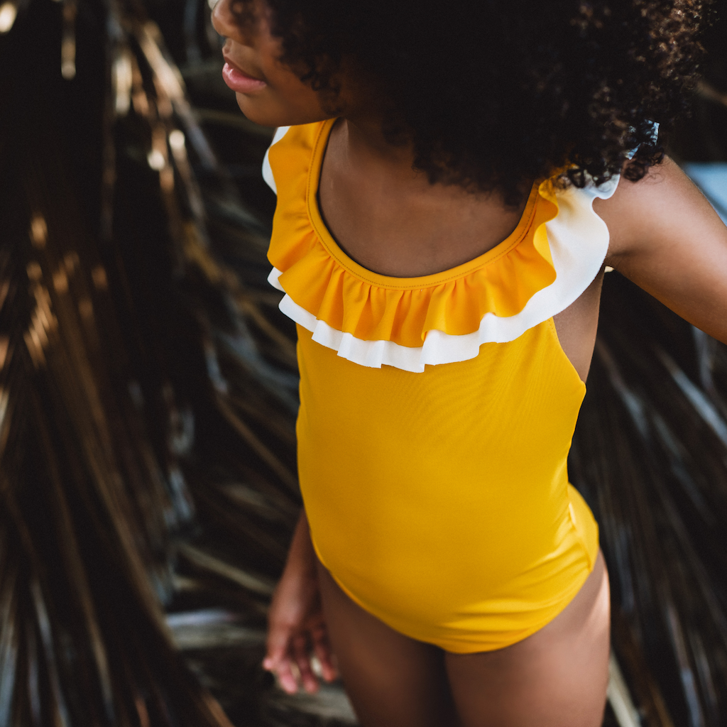 Girl wearing Folpetto penelope swimsuit for girls in mango yellow with white ruffle