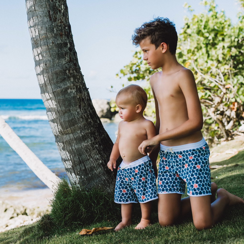 Boys wearing Folpetto Tommaso swim shorts for boys in teal blue and mandarin red tropical leaf print