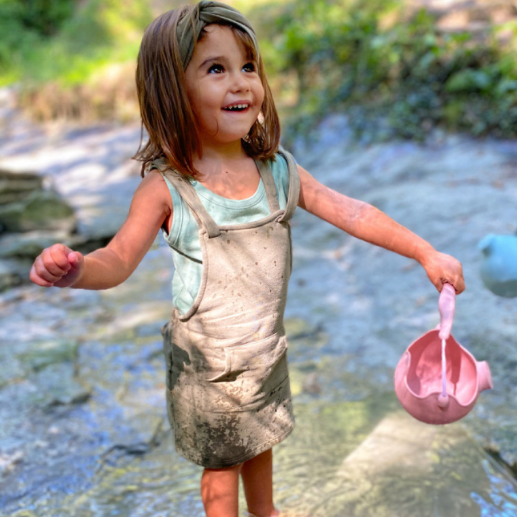 Little girl paddling in the stream with her Scrunch silicone watering can in old rose