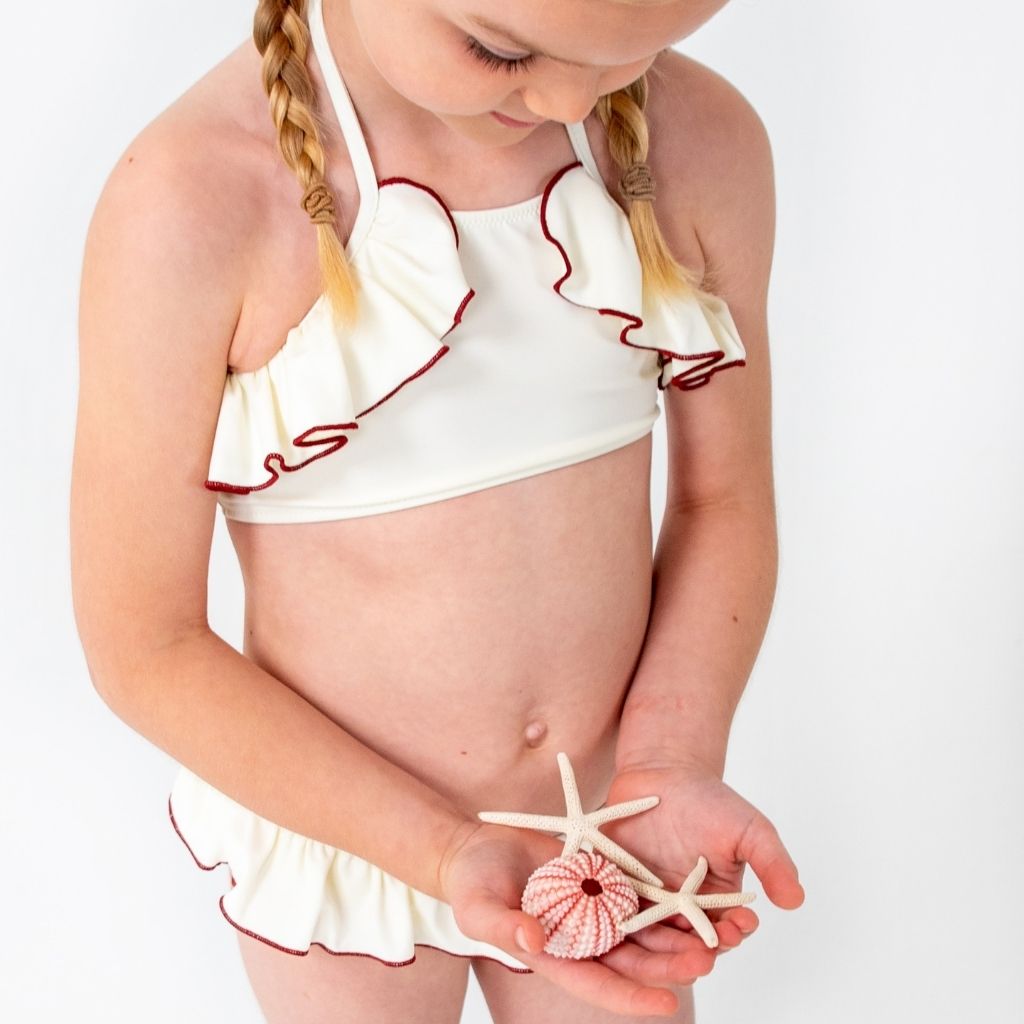 Little girl wearing Folpetto brand Leila Bikini in Ivory and Terracotta holding a starfish