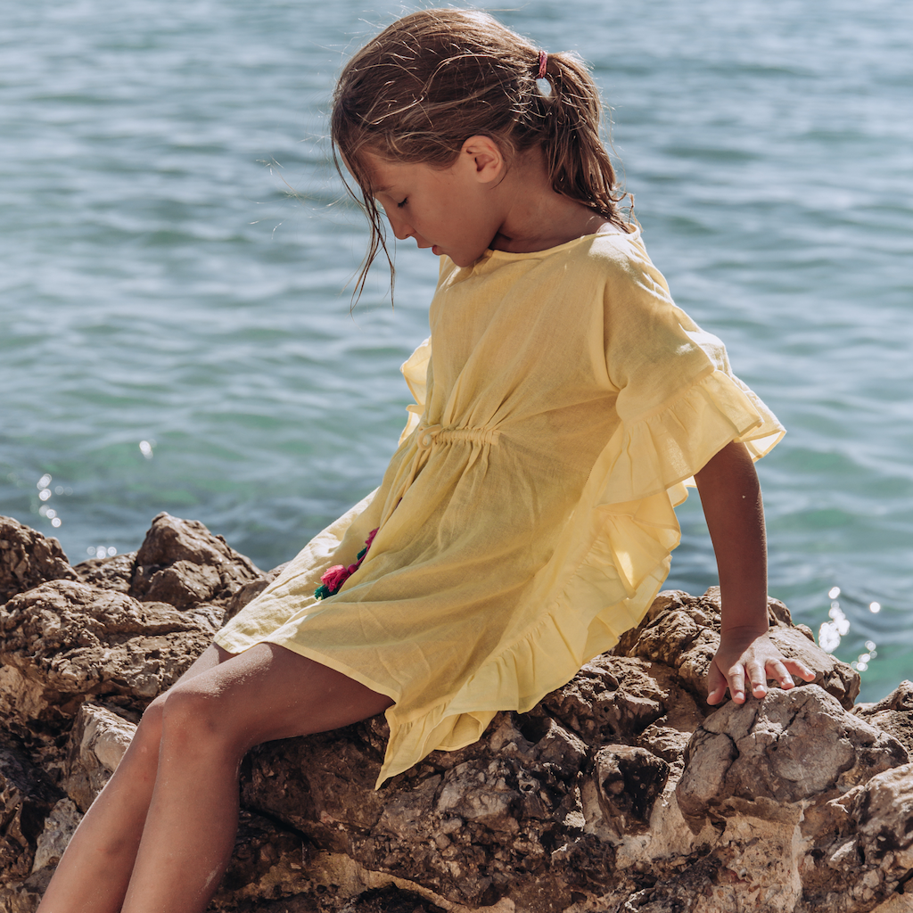 Little girl on the rocks wearing Lison Paris Lea Poncho cover-up in yellow