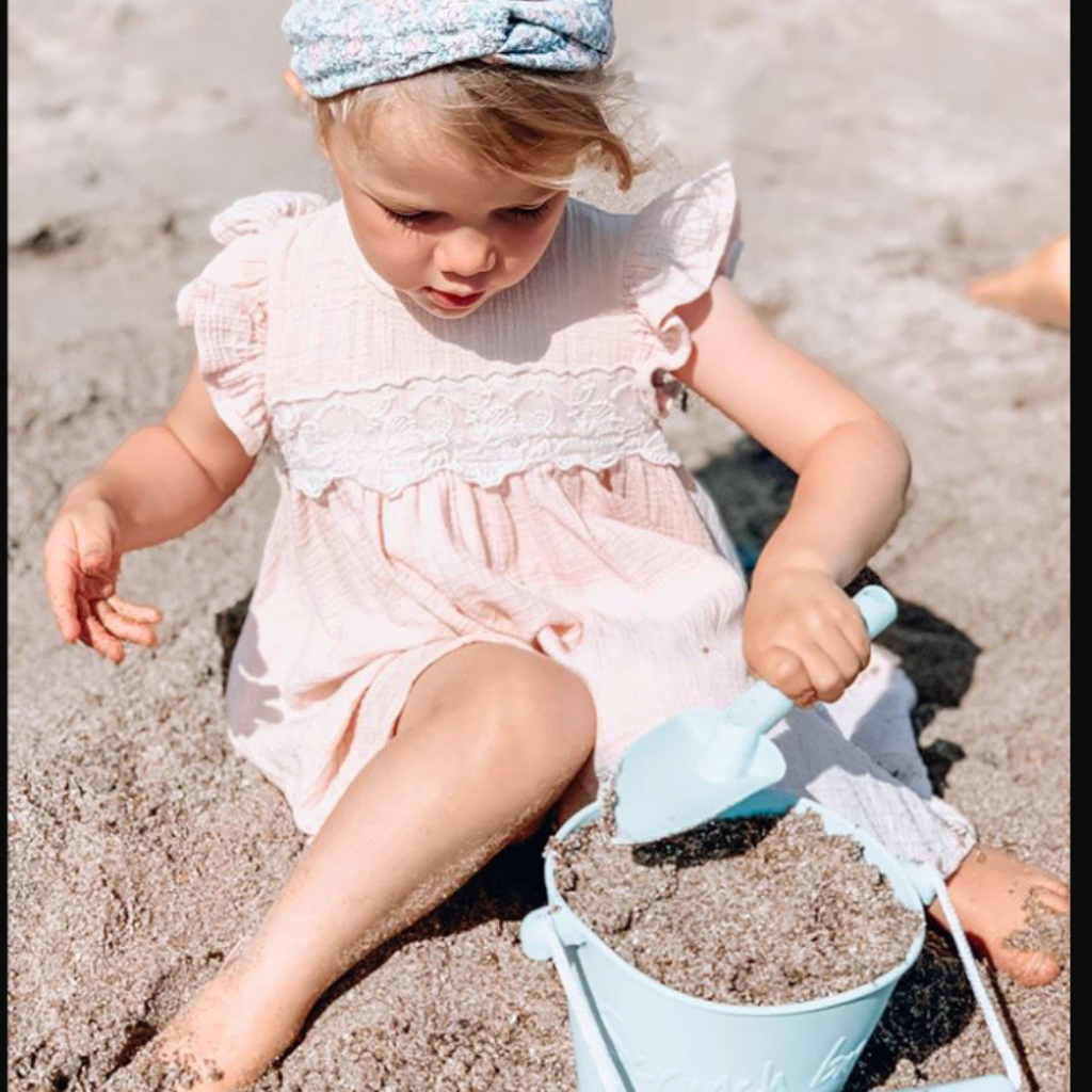 Little girl on the beach playing with scrunch silicone bucket and spade in duck egg blue