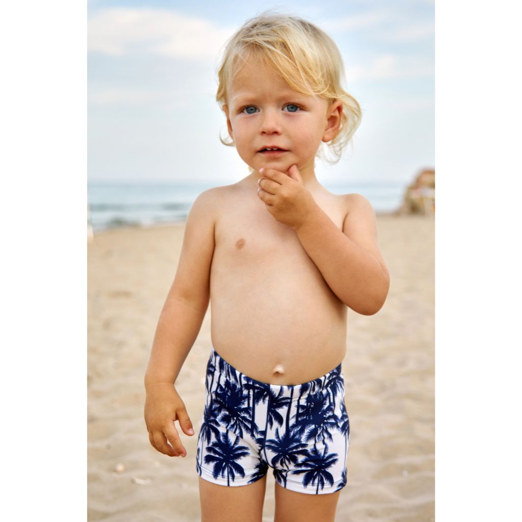 Little boy wearing Suncracy Palms Menorca Lycra Swim Shorts for Baby Boys featuring a Palm Tree print