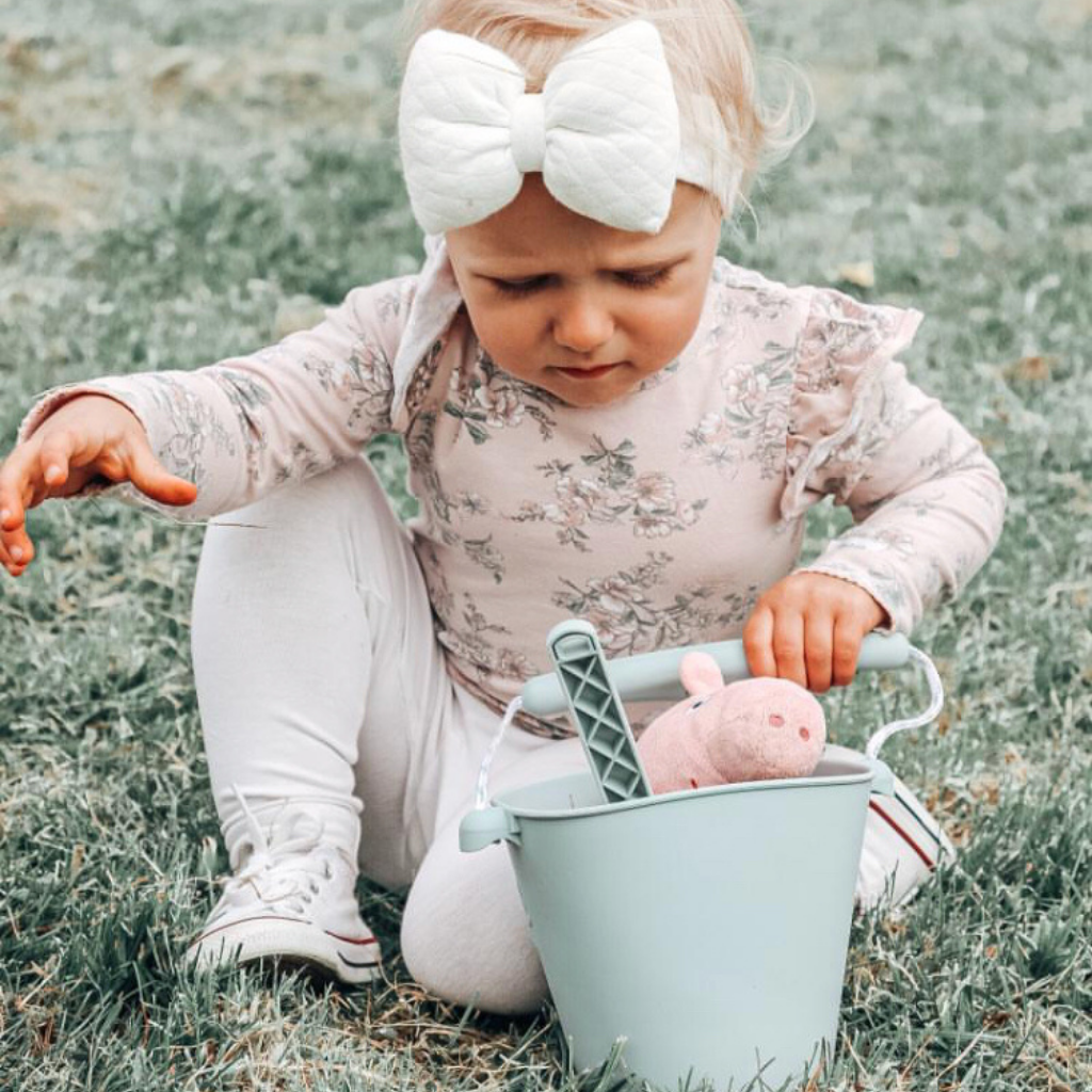 Little girl playing in the garden in with her scrunch silicone bucket and spade in sage green