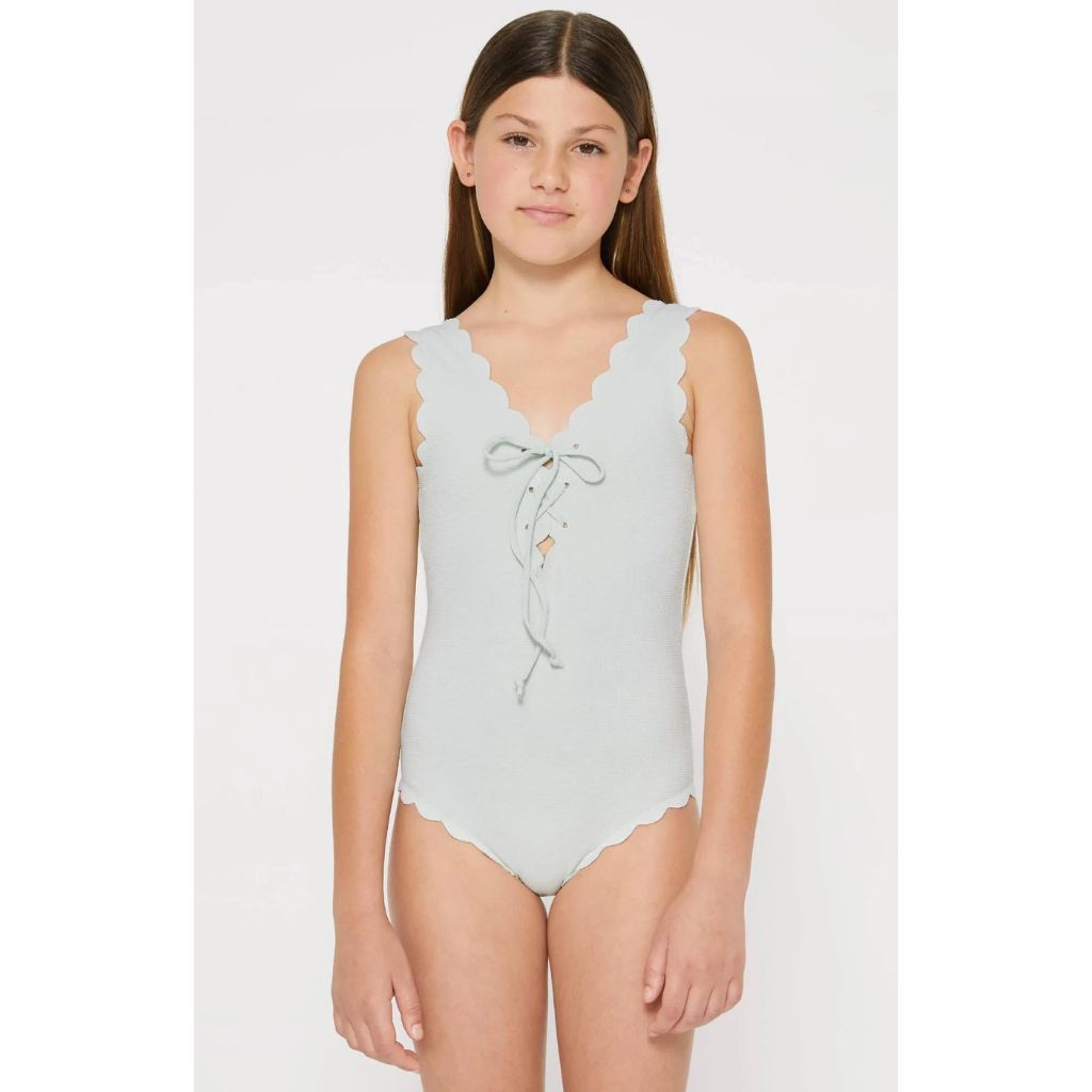 Girl wearing the Marysia Bumby Palm Springs Lace Up Reversible Swimsuit in Coconut Shell Print and Crystalline on the reverse