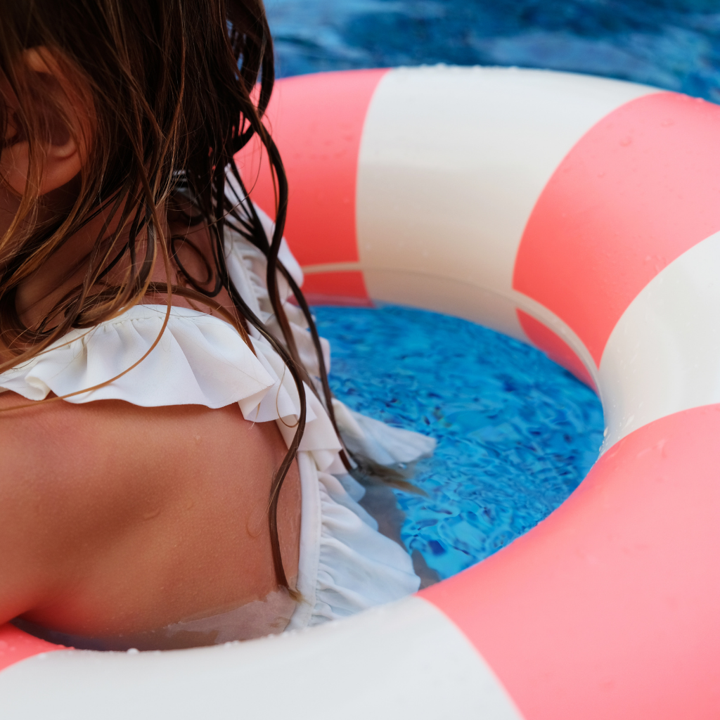 Little girl in Petites Pommes inflatable rubber ring in Sorbet coral and white stripe