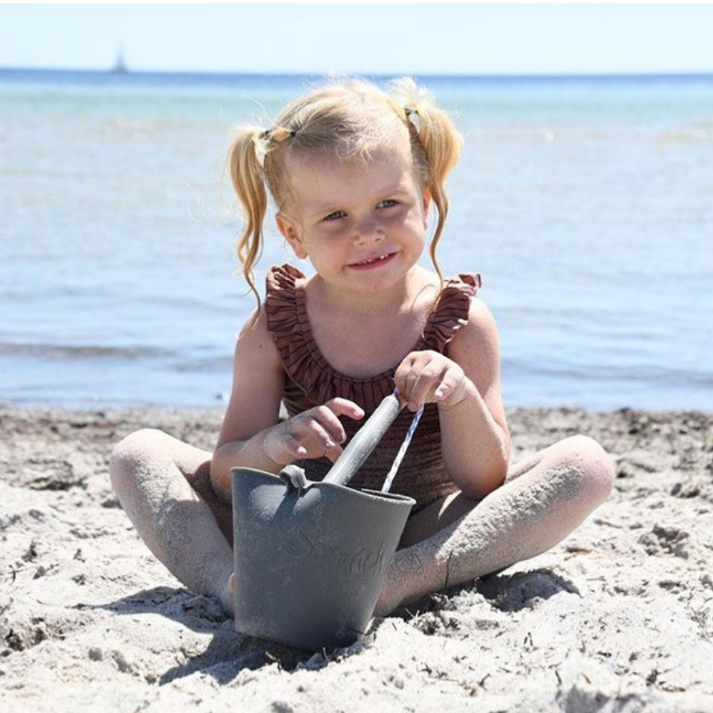 Little girl playing with scrunch bucket and spade in anthracite grey on the beach