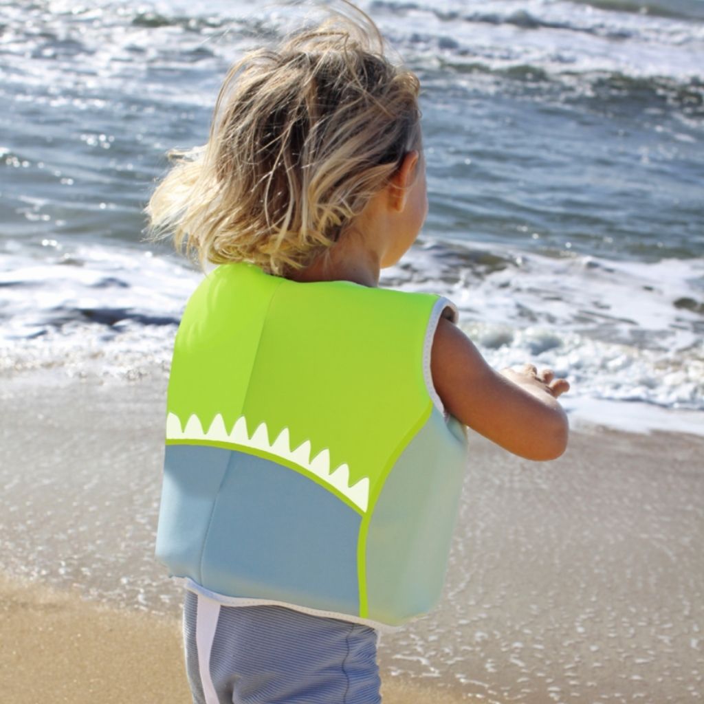 Little boy running into the sea wearing Sunnylife Kids swim float vest EU design in Shark Tribe khaki