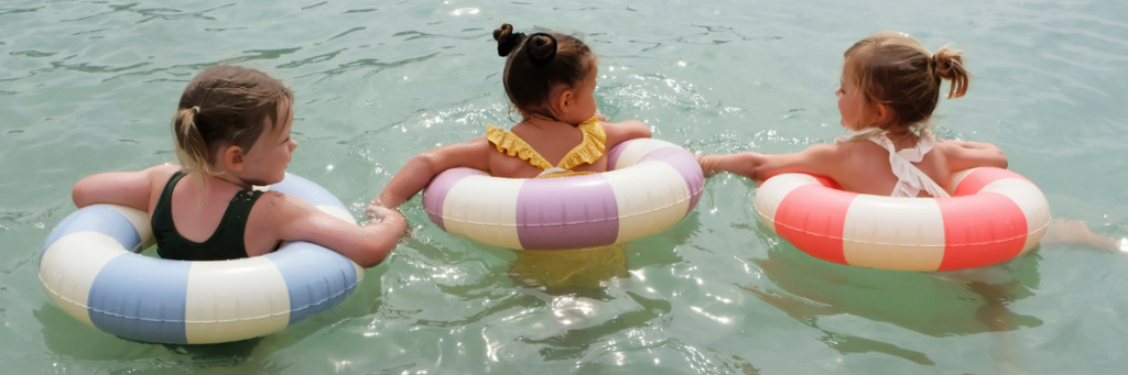 Little girls enjoying the sea in their Petites Pommes striped inflatable pool floats 