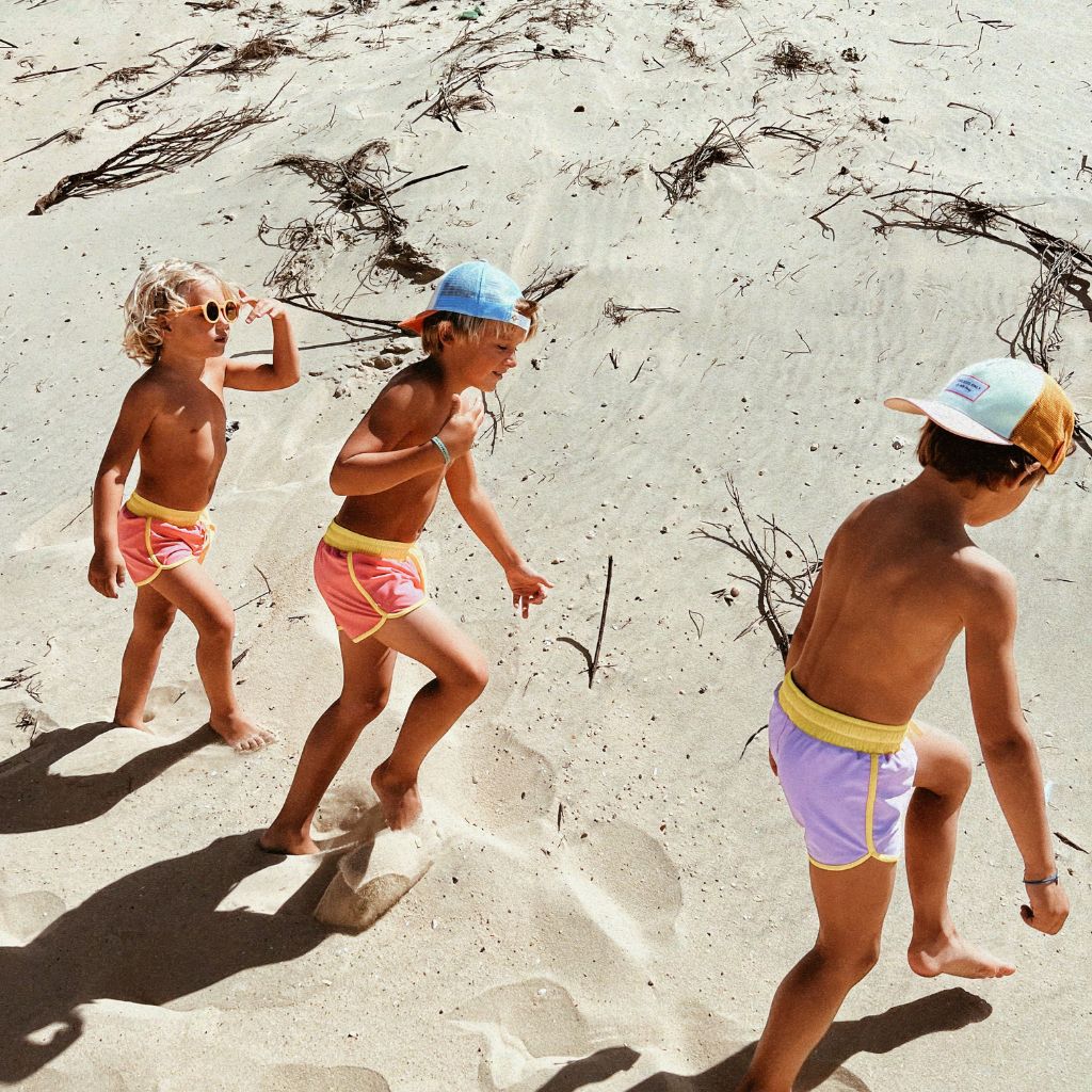 Boys on the beach wearing the Kiwi Unisex Swim Shorts in Lilas Purple from Baines Collection