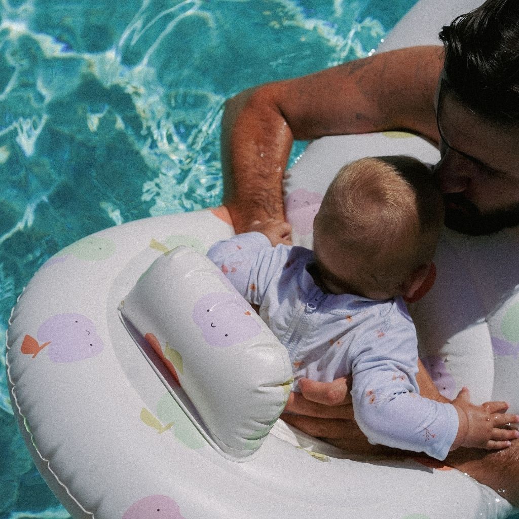 Close up of dad and baby using the Sunnylife Float Together Baby Seat in Apple Sorbet