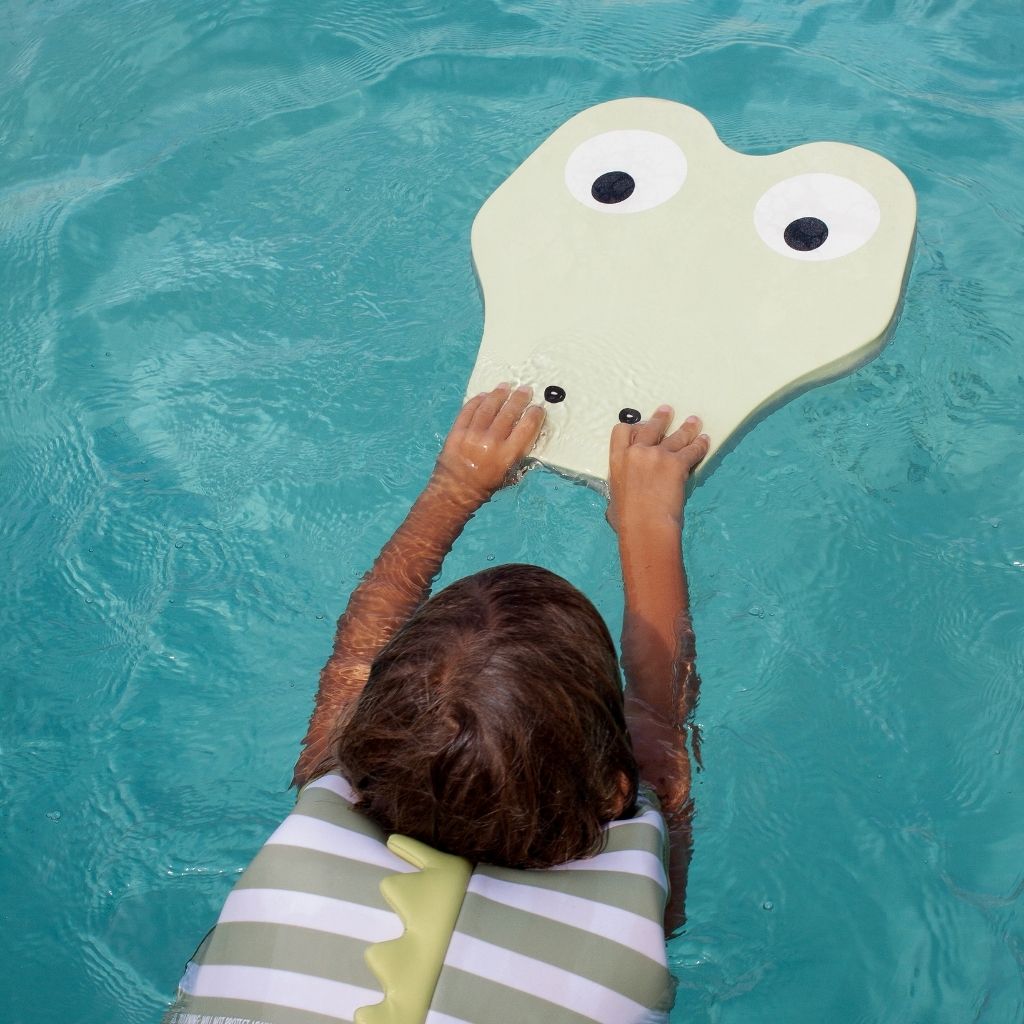 Little boy in the water using the Sunnylife Kids Kickboard Float in the Cookie the Croc shape