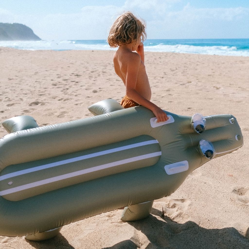 Little boy on the beach carrying the Sunnylife Cookie the Croc lie-on inflatable float in khaki green