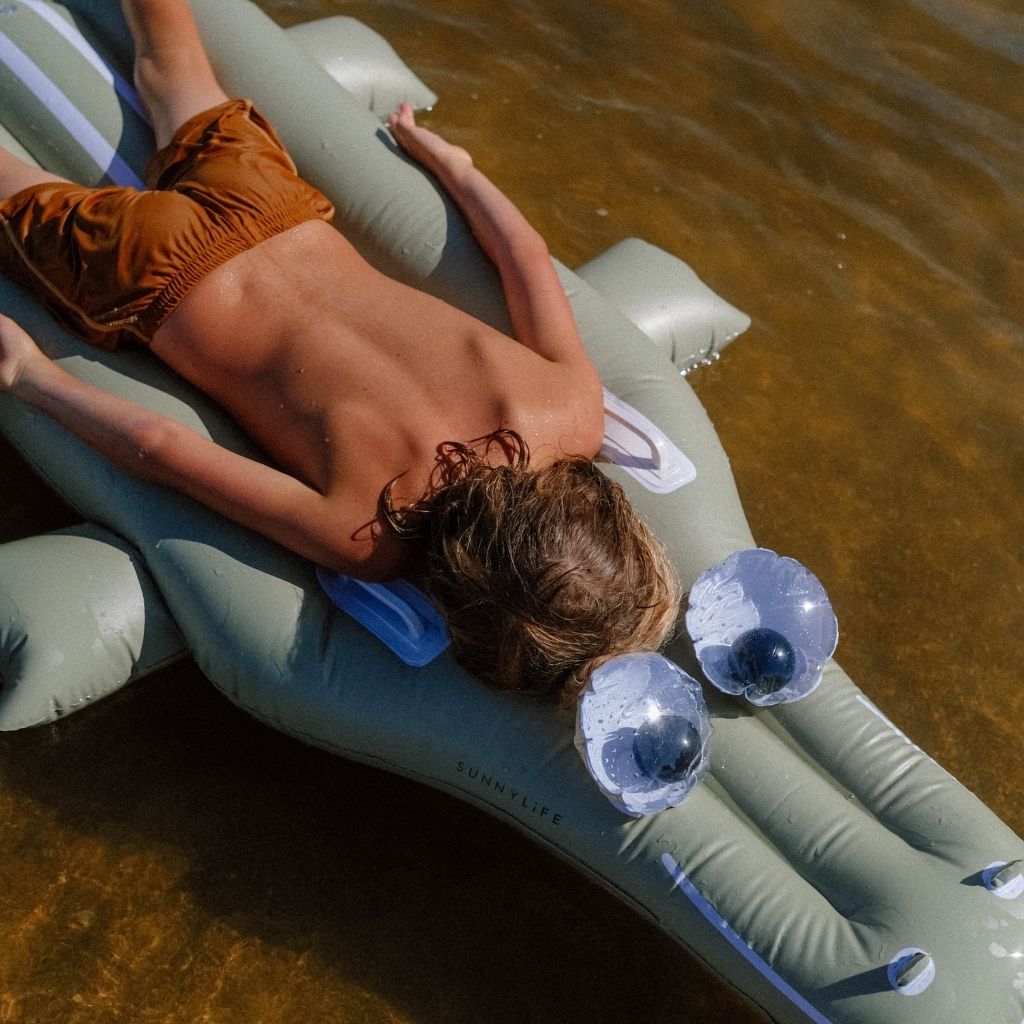 Little boy lying in the sea on the Sunnylife Cookie the Croc lie-on inflatable float in khaki green