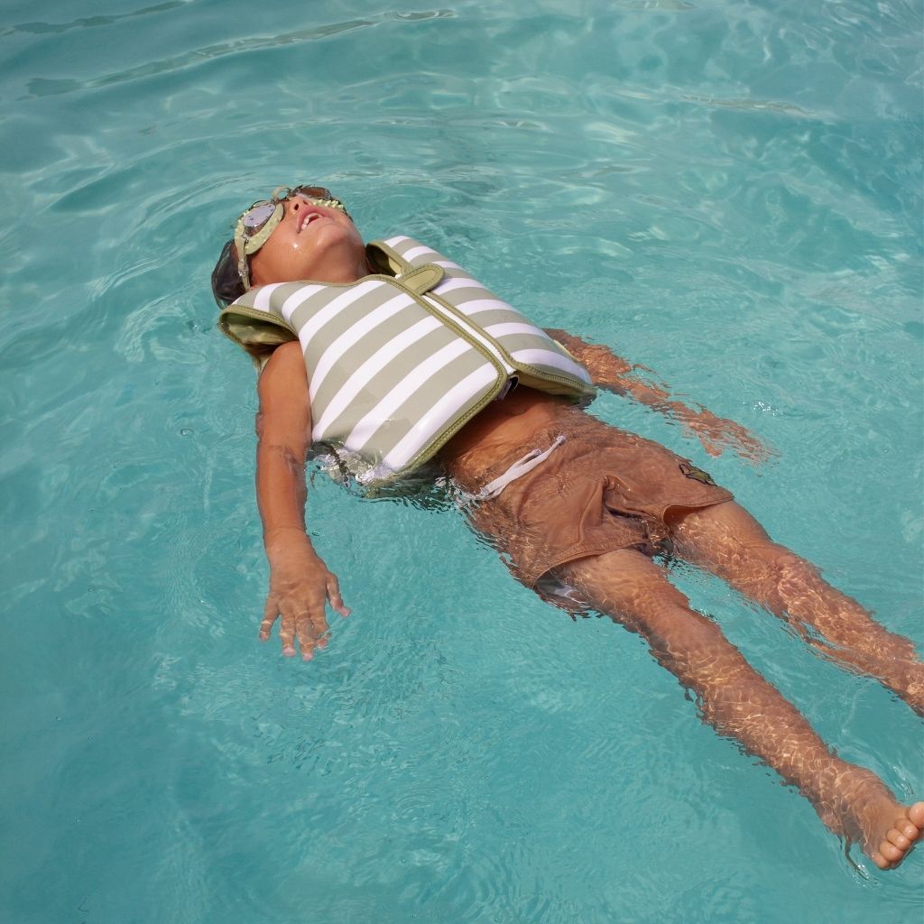 Little boy floating in the water wearing his Sunnylife Into The Wild Swim Vest
