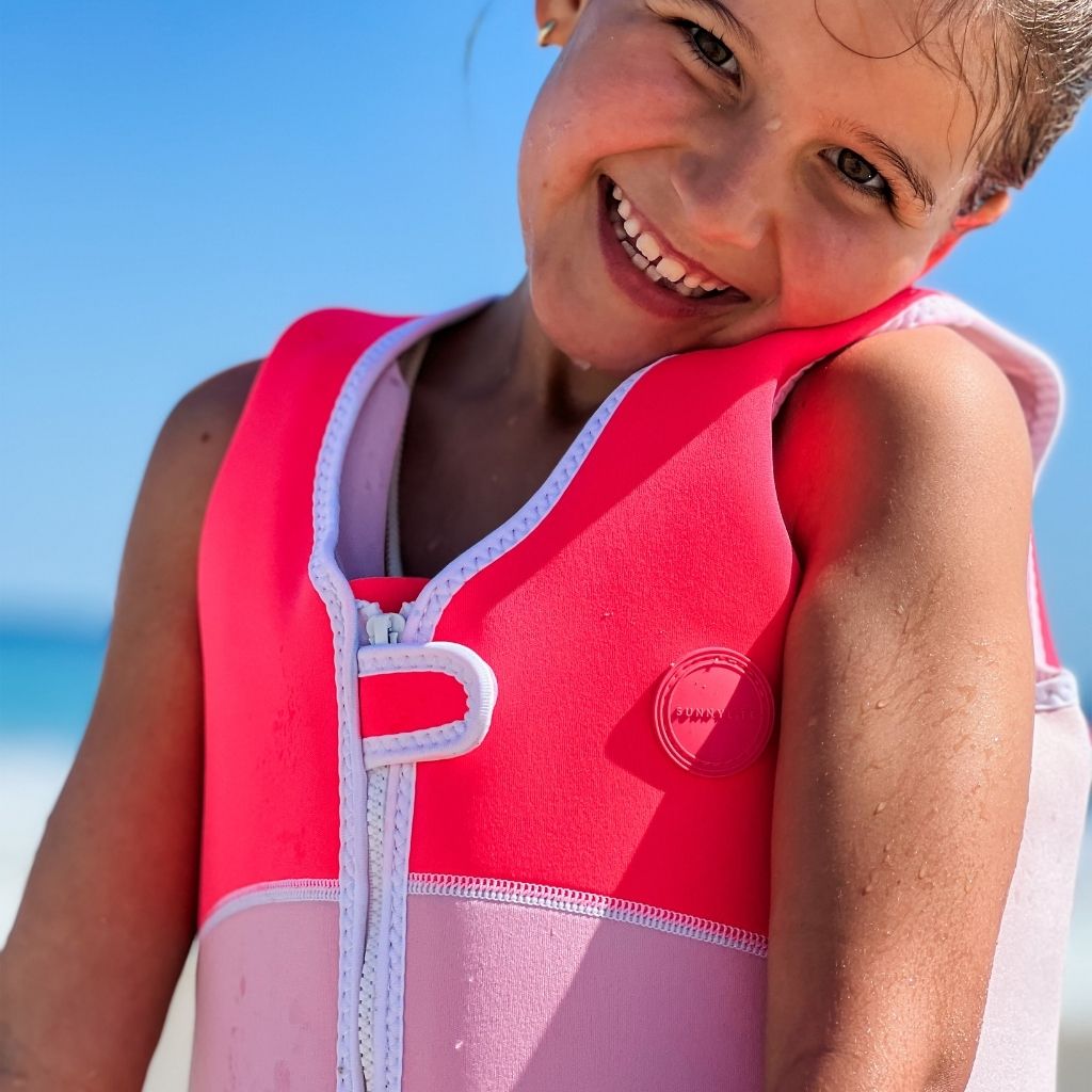 Close up shot of a little girl wearing the Sunnylife Kids Melody the Mermaid swim vest in neon strawberry