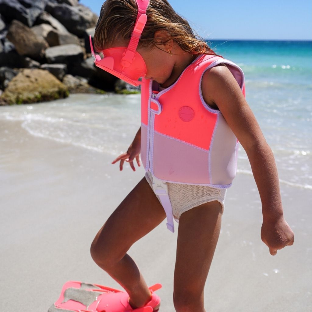 Little girl about to go swimming wearing the Sunnylife Kids Melody the Mermaid swim vest in neon strawberry