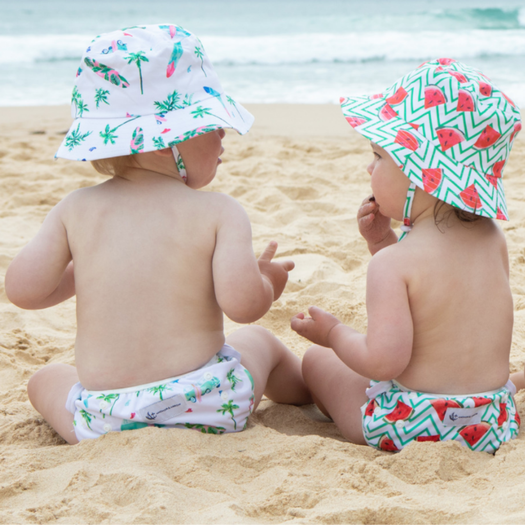 Two babies chatting on the beach wearing Anchor & Arrow Chasing Waves and Frolicking Watermelon print unisex reusable swim nappy