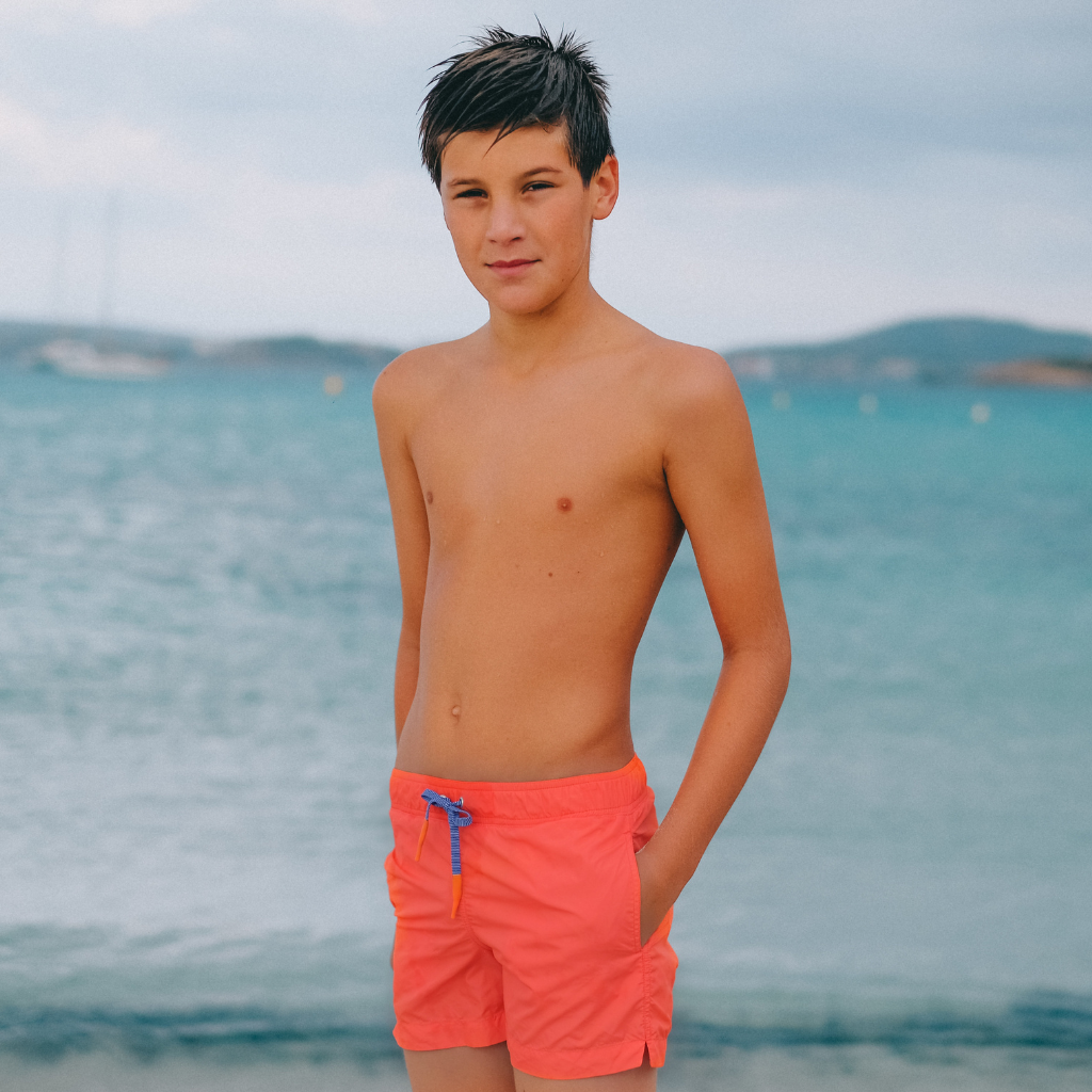 Boy wearing Lison Paris Capri Swim Shorts in Clementine Orange