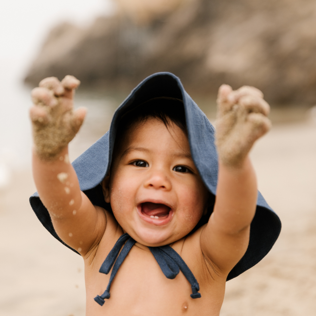 Little boy having fun on the beach wearing Briar Baby sun hat in navy blue Cove