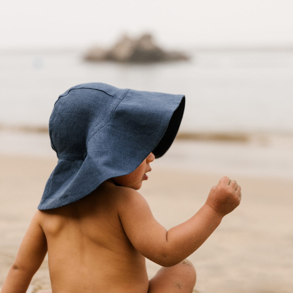Little boy on the beach showing side view of the Briar Baby sun hat in navy blue Cove