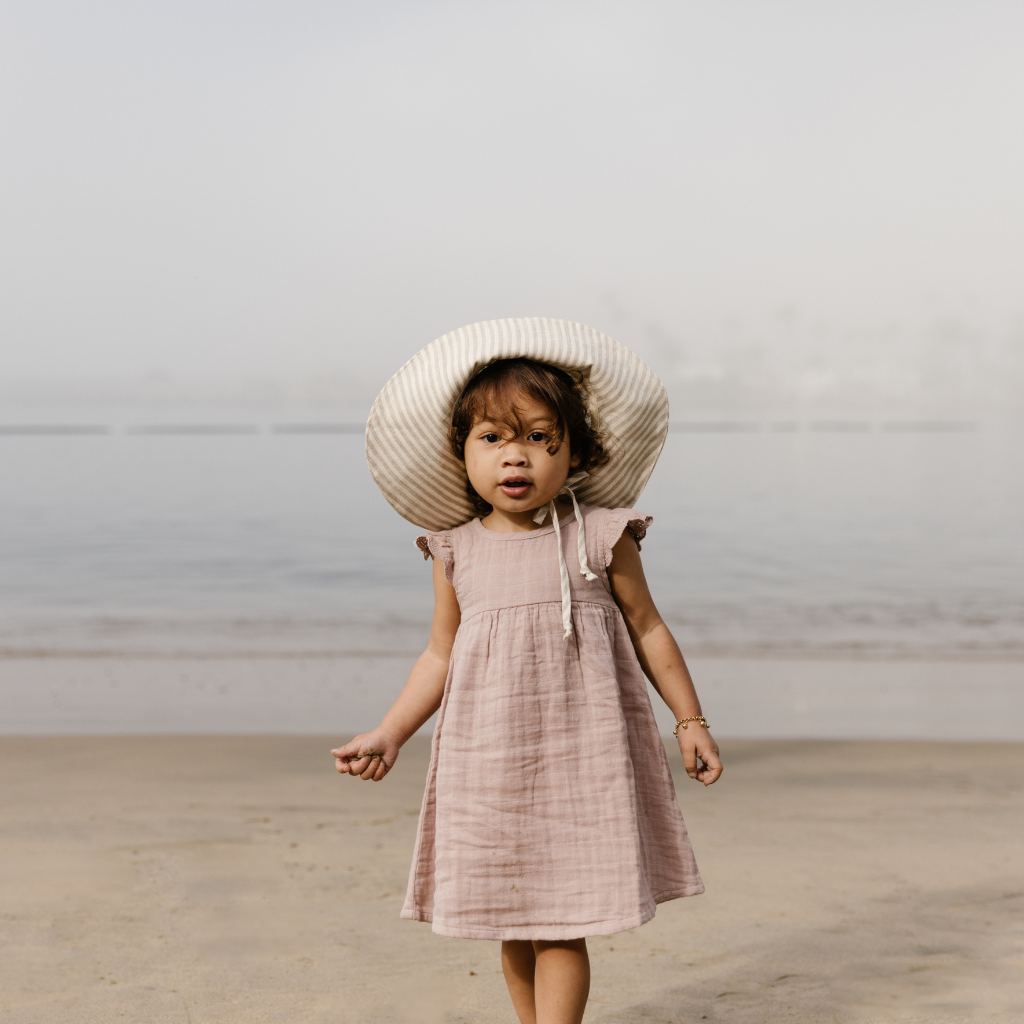 Little girl facing the camera wearing a Briar Baby sun hat in beige and grey Harbor Stripe