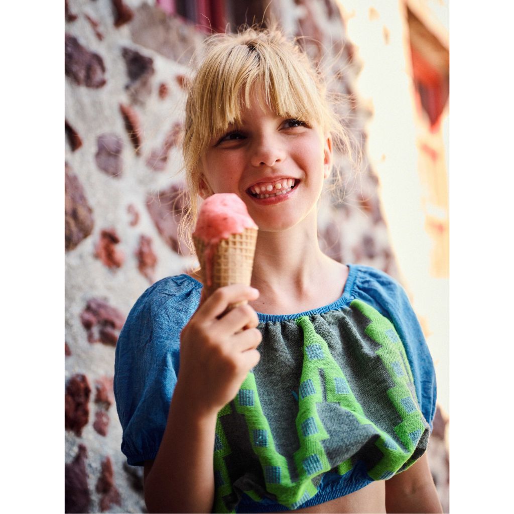 Little girl having an ice cream whilst wearing the Devotion Twins Stars Dafni blouse top in denim blue and neon green