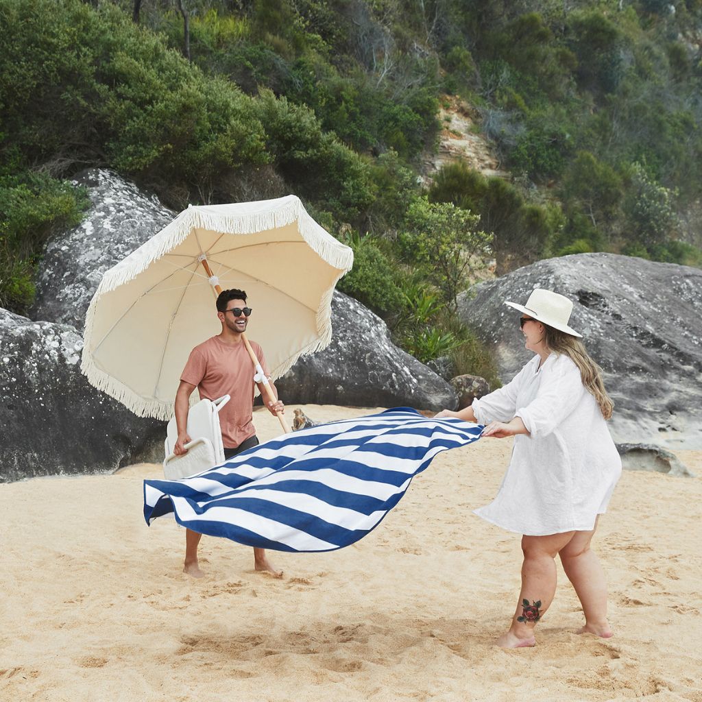 Couple on the beach laying out their Dock and Bay cabana round beach towel in Whitsunday Blue