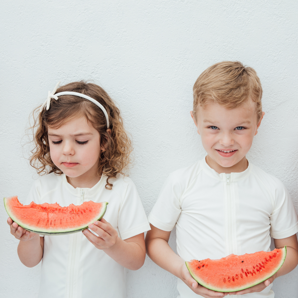 Little girl and boy eating watermelons wearing Folpetto white short-sleeved rash guard