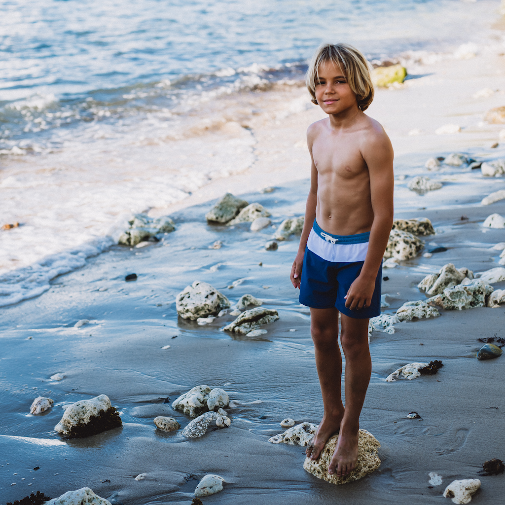 Boy by the sea wearing Folpetto Harry swim shorts for boys in blue