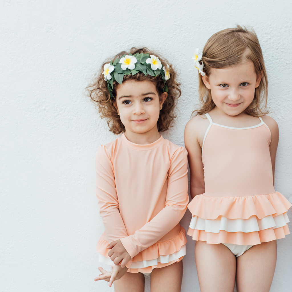 Little girls wearing Folpetto Amelia swimsuit and Lucie rash guard  in peach pink