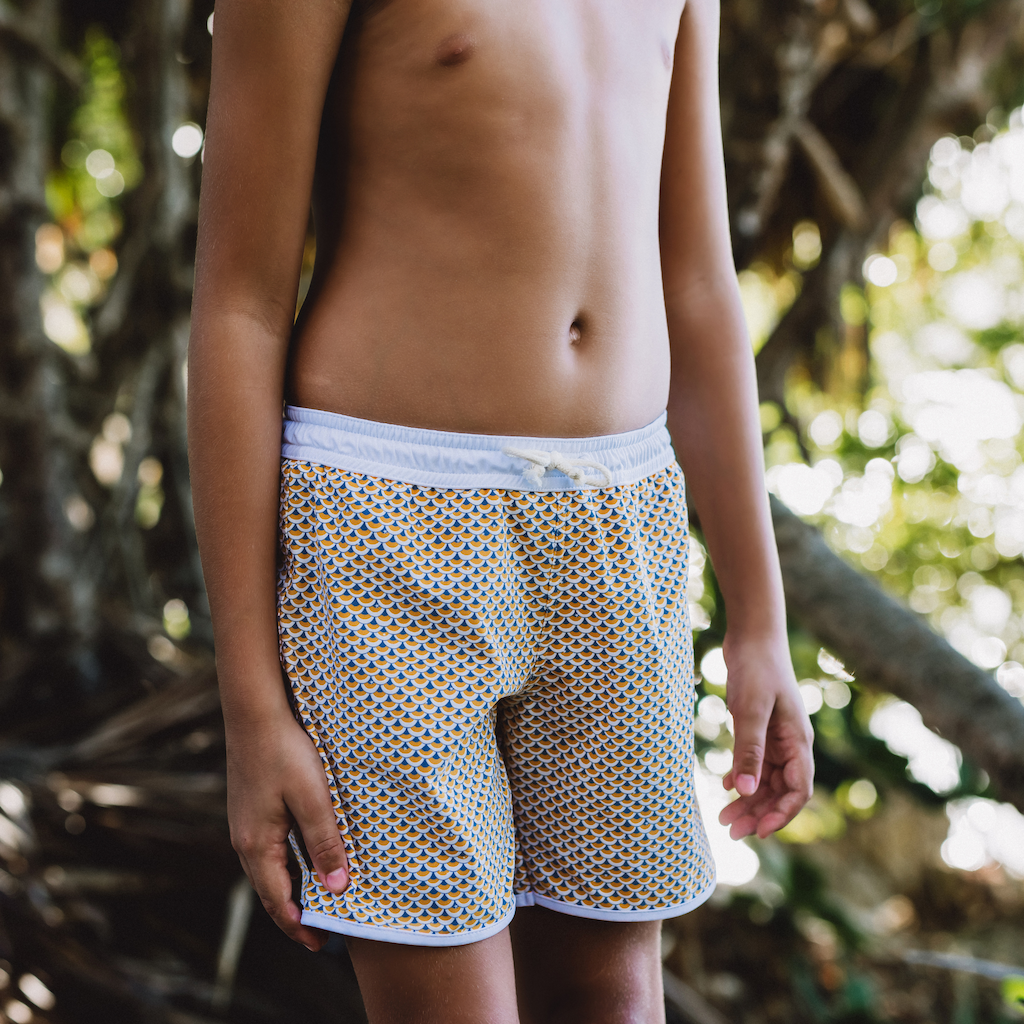Boy wearing Folpetto Tommaso swim shorts for boys in mango yellow and pebble grey scales print