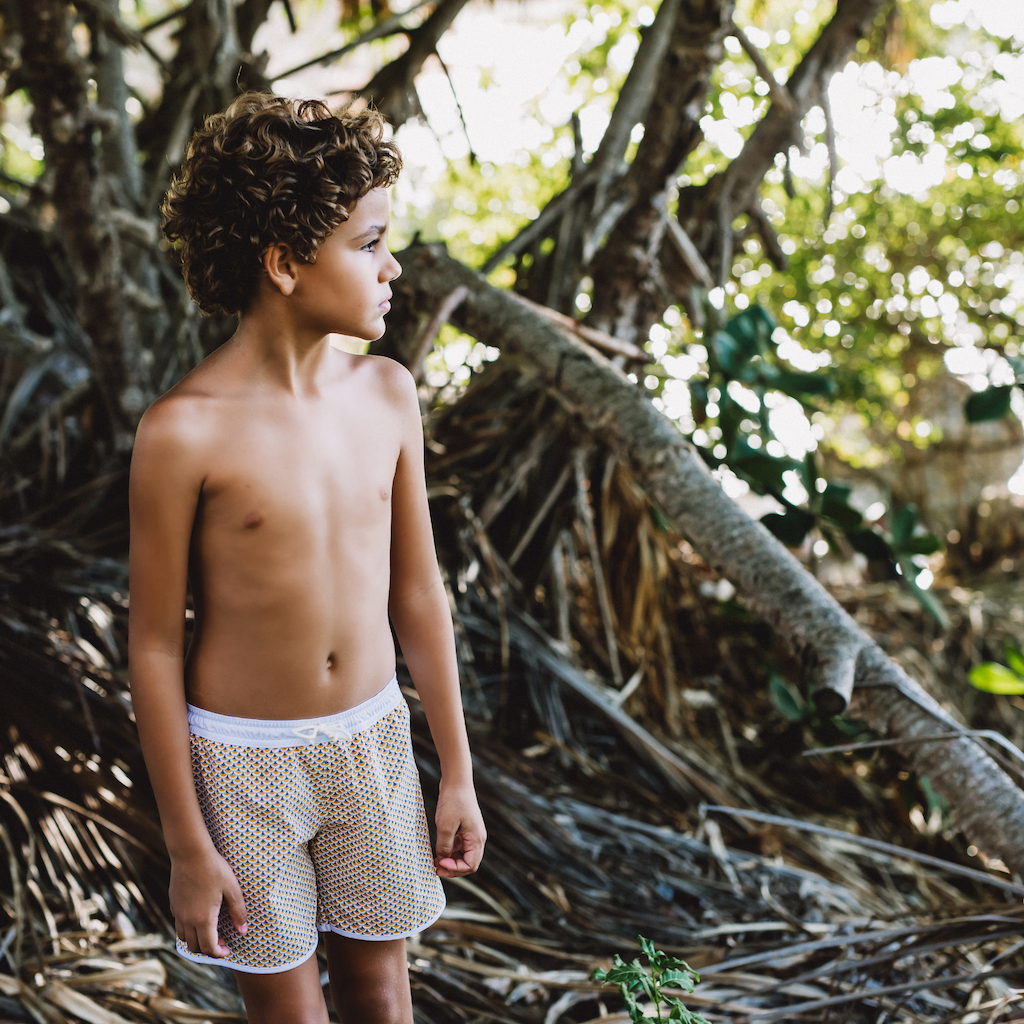 Boy wearing Folpetto Tommaso swim shorts for boys in mango yellow and pebble grey scales print