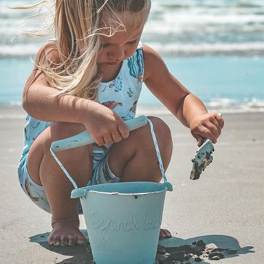Little girl playing with Scrunch silicone bucket and spade in duck egg blue on the beach