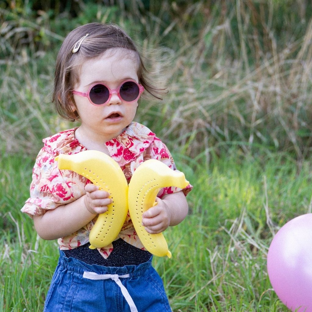 Little girl carrying bananas and wearing Ki et La Woam round sunglasses in Strawberry Pink