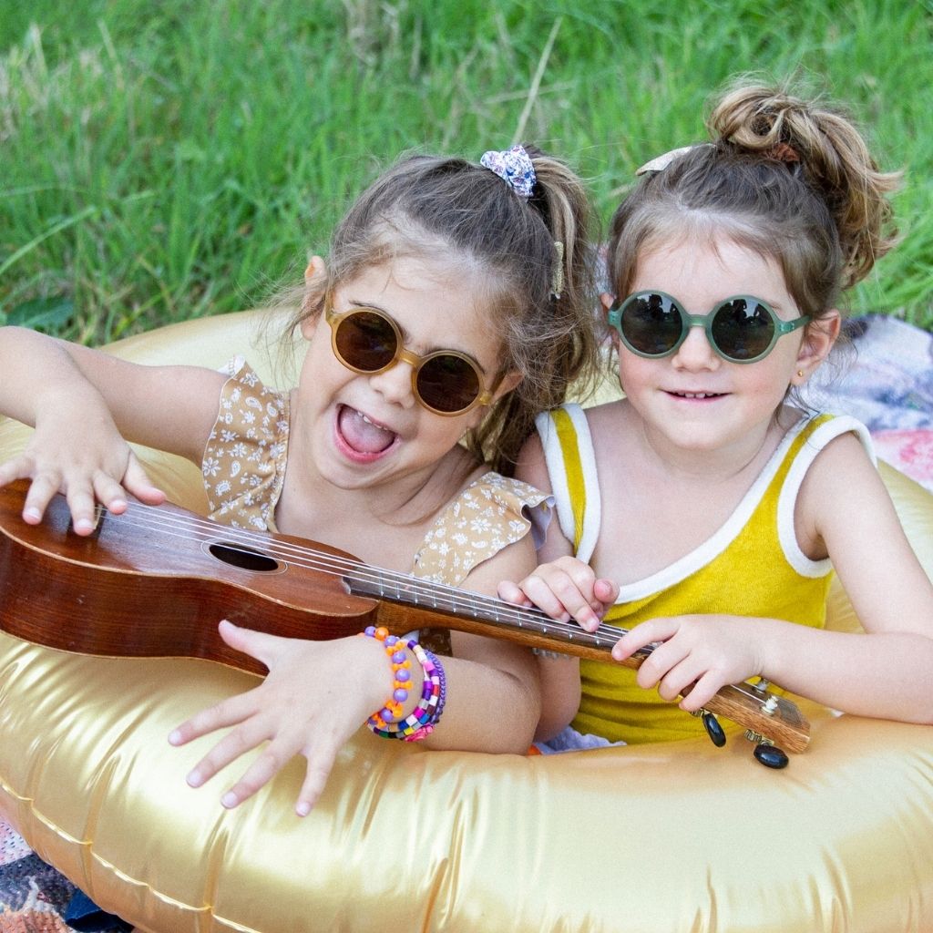Little girls playing with guitar wearing Ki et La Woam round sunglasses in Bottle Green and Brown