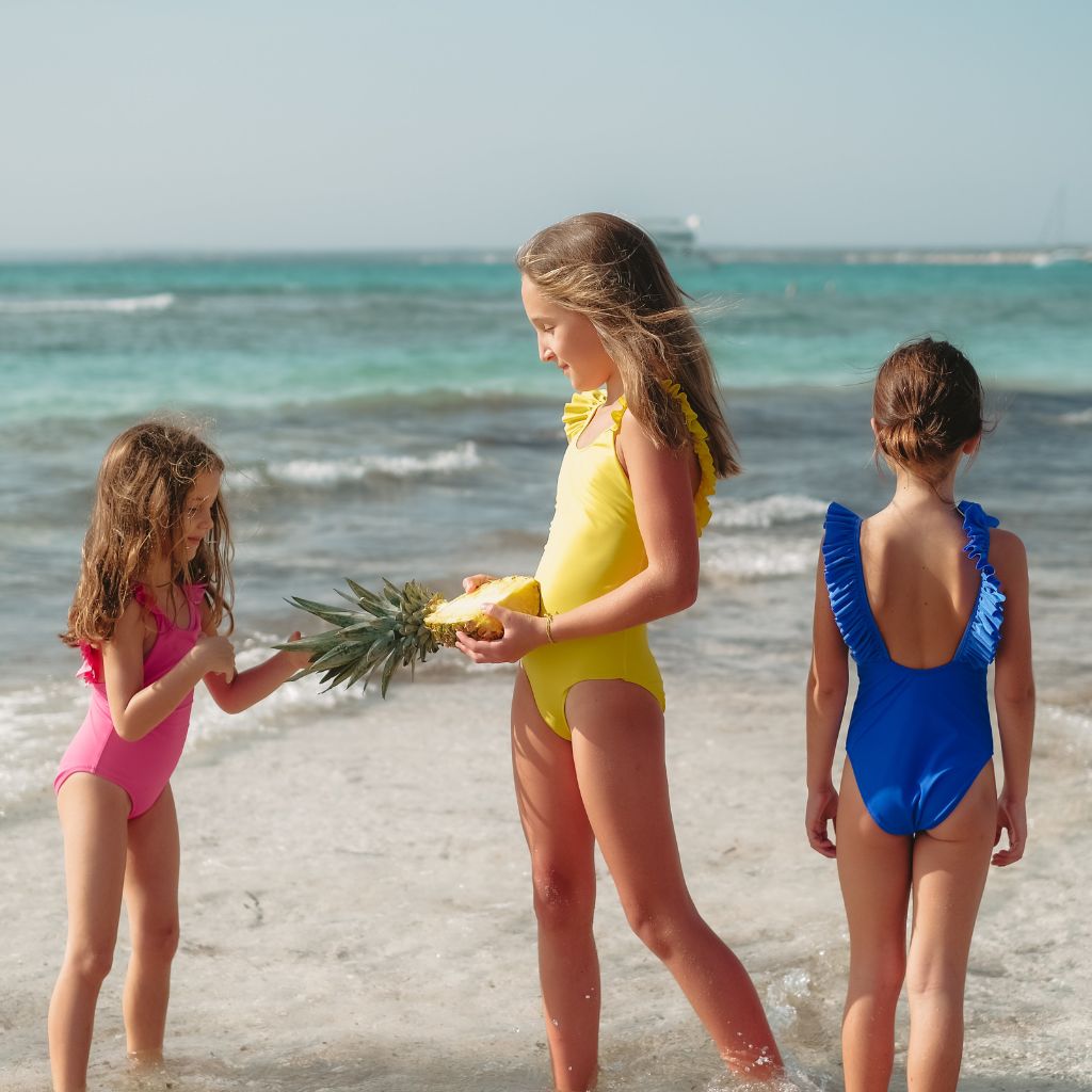 Little girl on the beach wearing the Lison Paris best-selling girl's swimsuit Bora Bora in candy pink, Azur blue and lemon yellow
