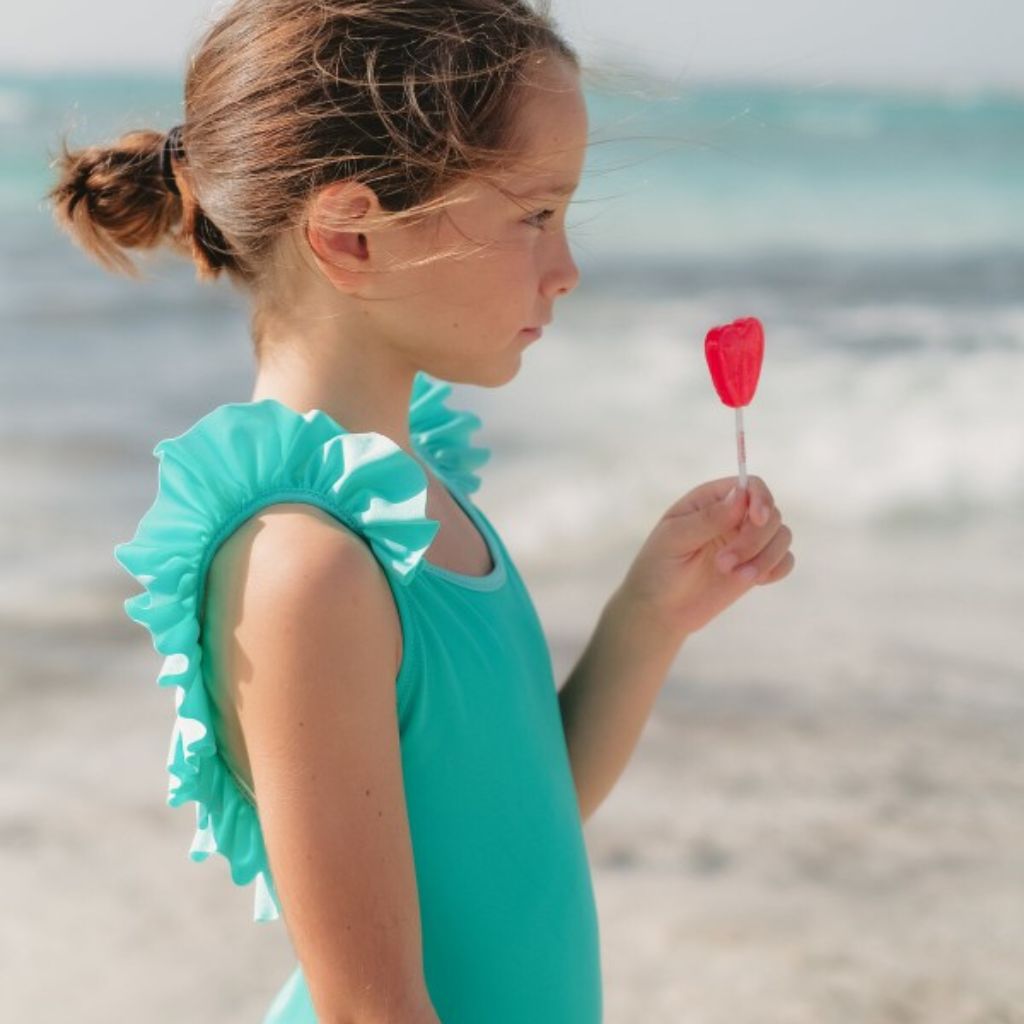 Little girl with a heart lollipop wearing Lison Paris Girls Bora Bora Swimsuit in Mint Green